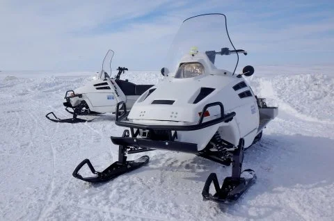 Two white snowmobiles parked on snow.
